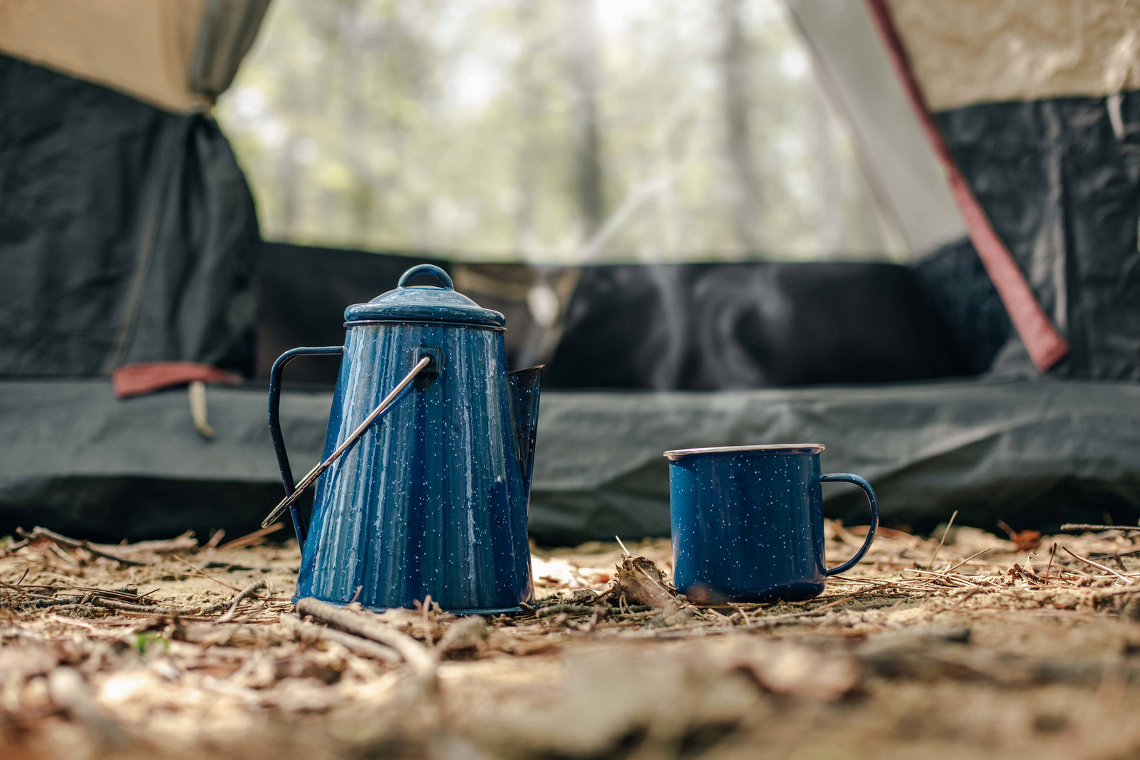 Blue metal enamelware kettle and cup in front of a tent.